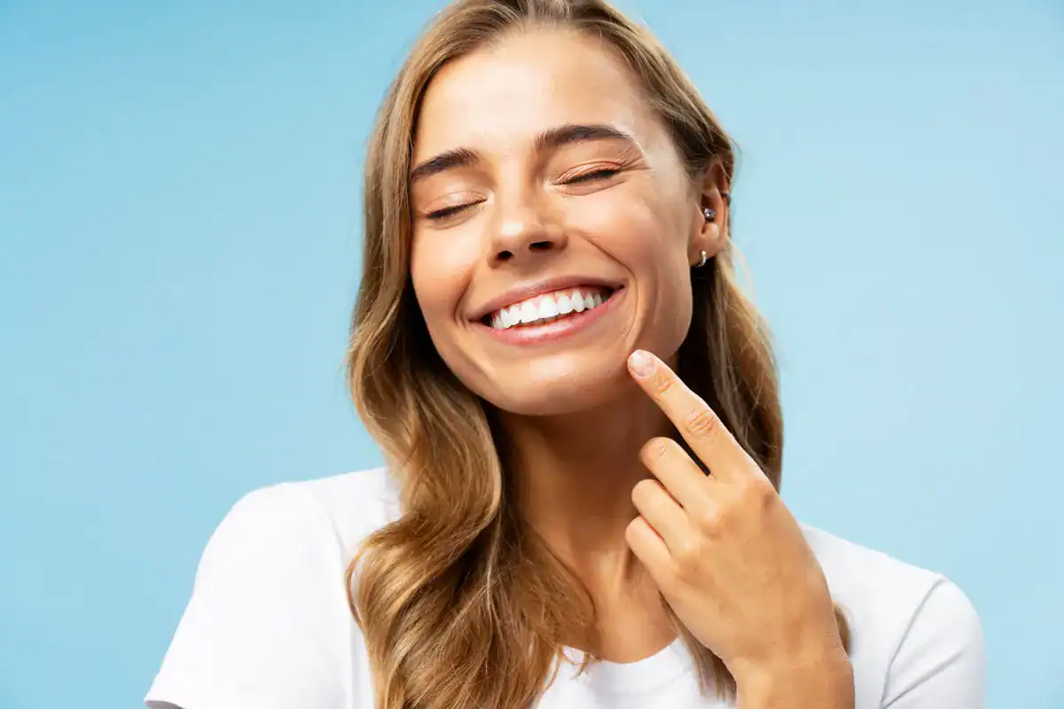 A smiling woman pointing to her teeth, showcasing dental health and confidence.